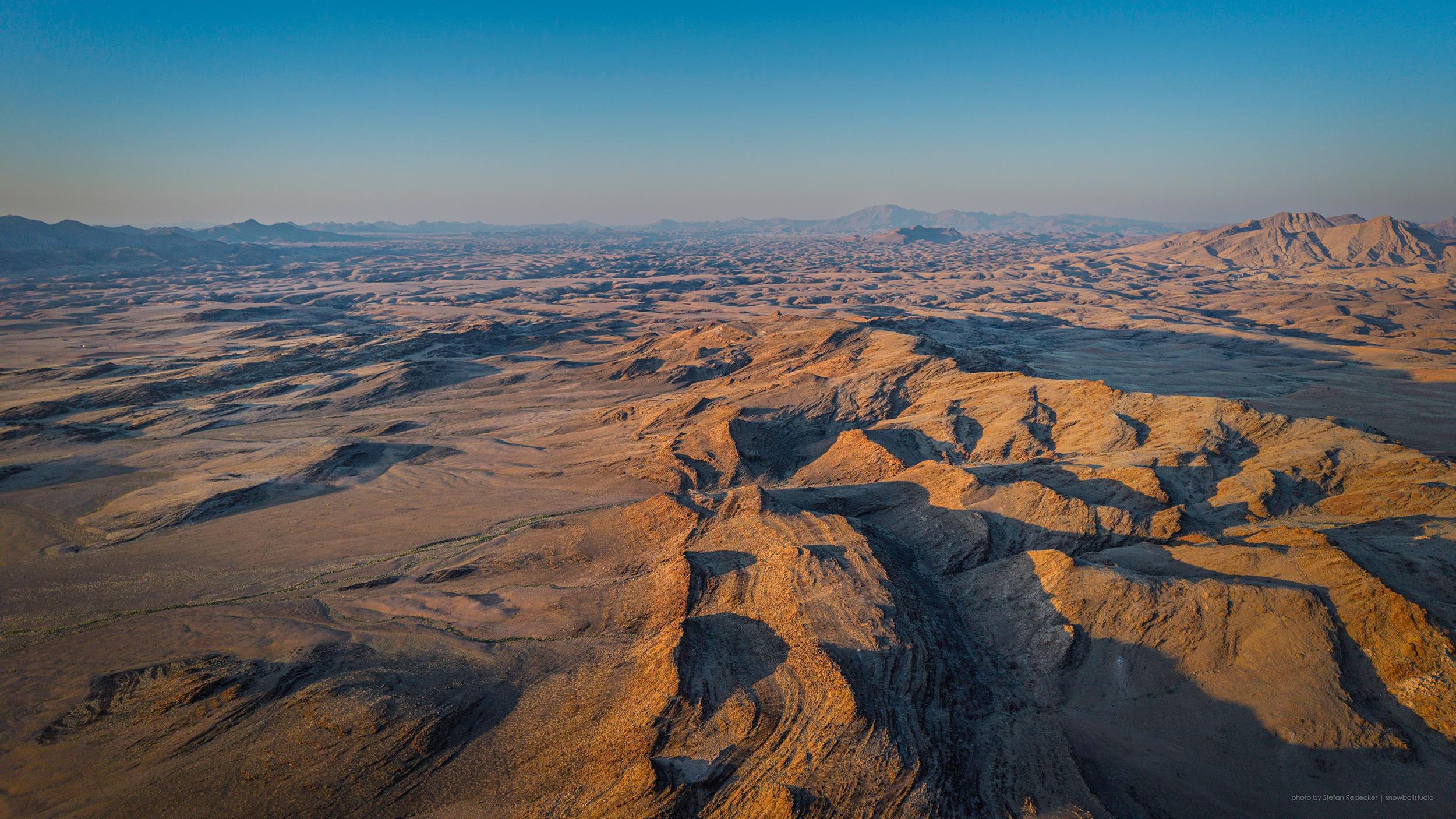 Dramatic Namib Desert sunrise with golden and red hues painting the sand dunes and rocky plains