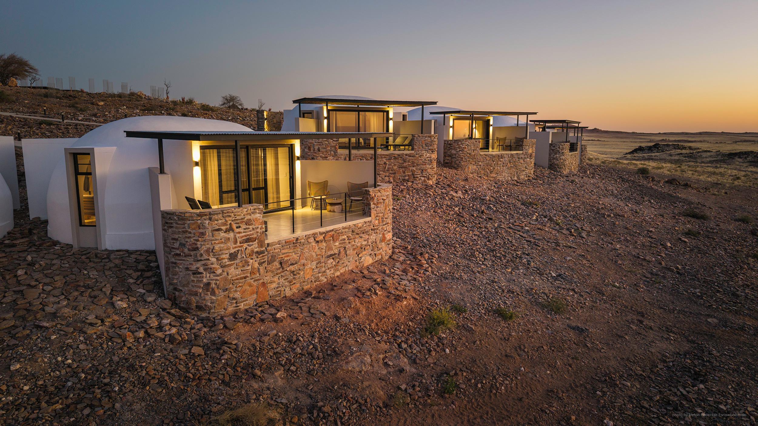 Luxury desert chalet interior with panoramic terrace overlooking Namib Desert waterhole at sunset