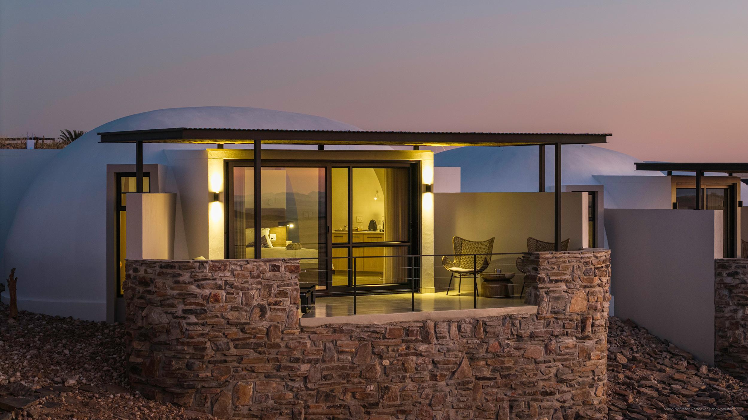 Spacious luxury chalet bedroom with desert view through large windows and natural stone walls