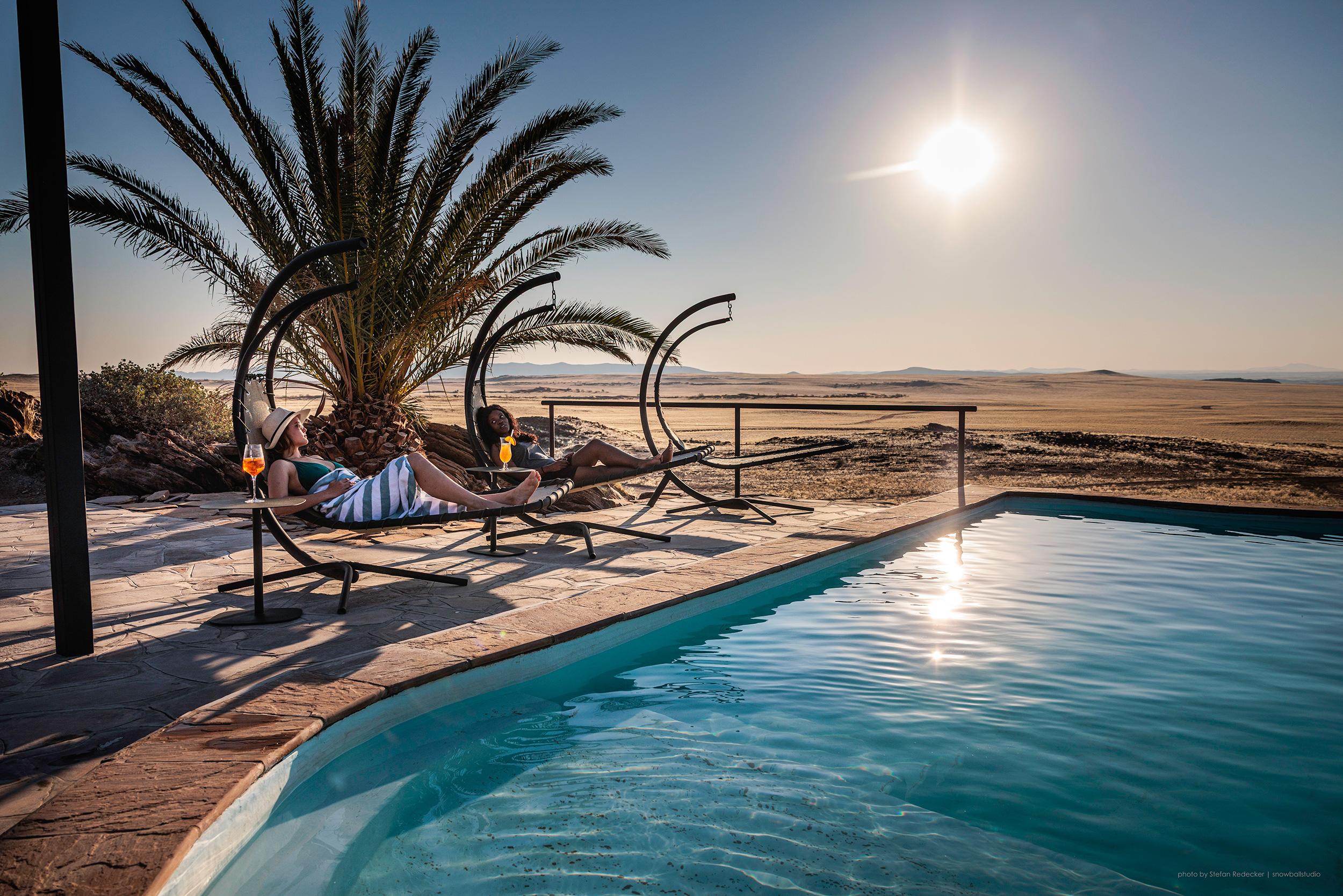 Infinity pool with panoramic view over golden desert plains and mountain range at sunset